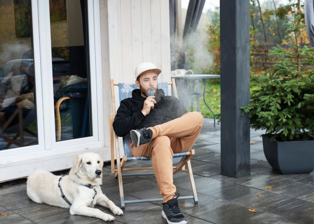 Man vaping with his dog on a patio.